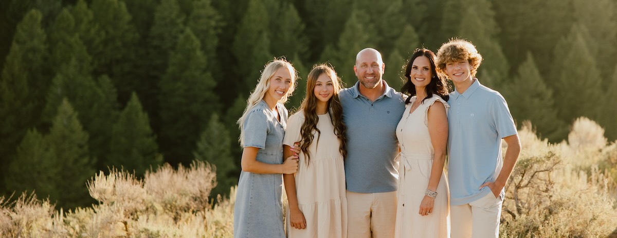 The Mortensen Family standing outside in front of a hill with many trees